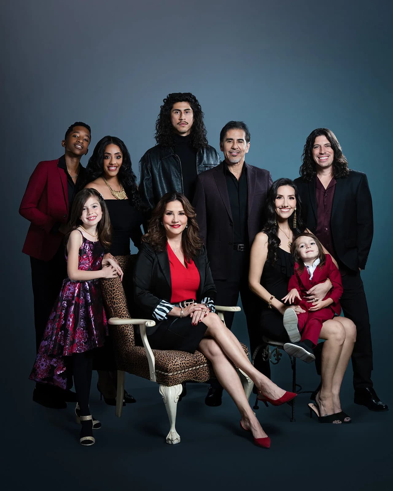 Extended family in red and black formal clothing against a deep blue studio backdrop