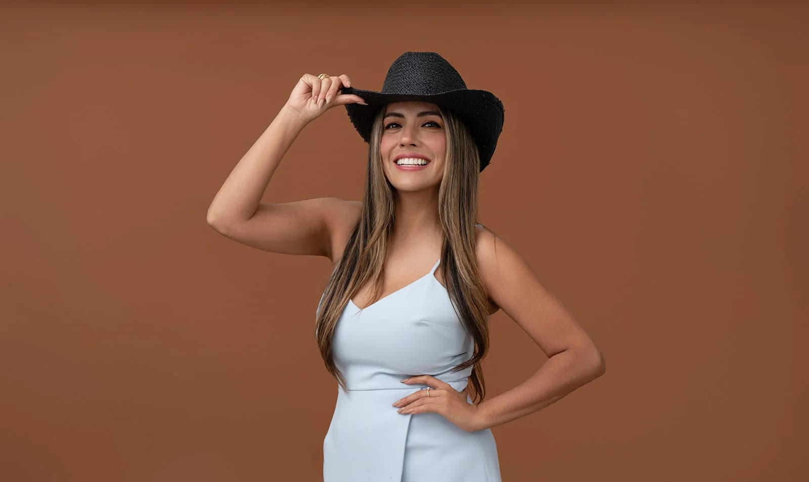 Woman in a black hat posing against a warm brown studio backdrop