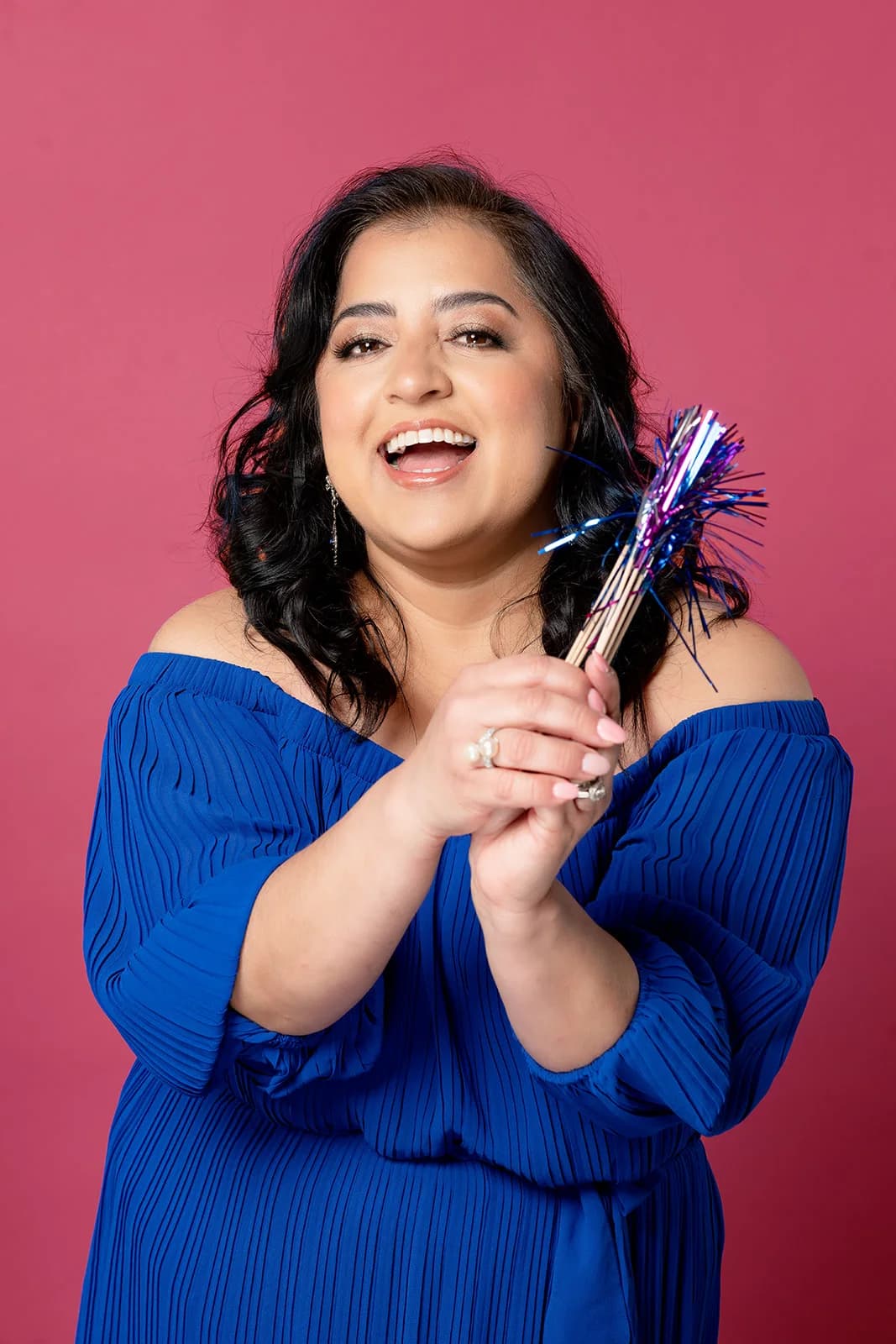 Woman in a blue dress holding metallic party decorations against a coral backdrop