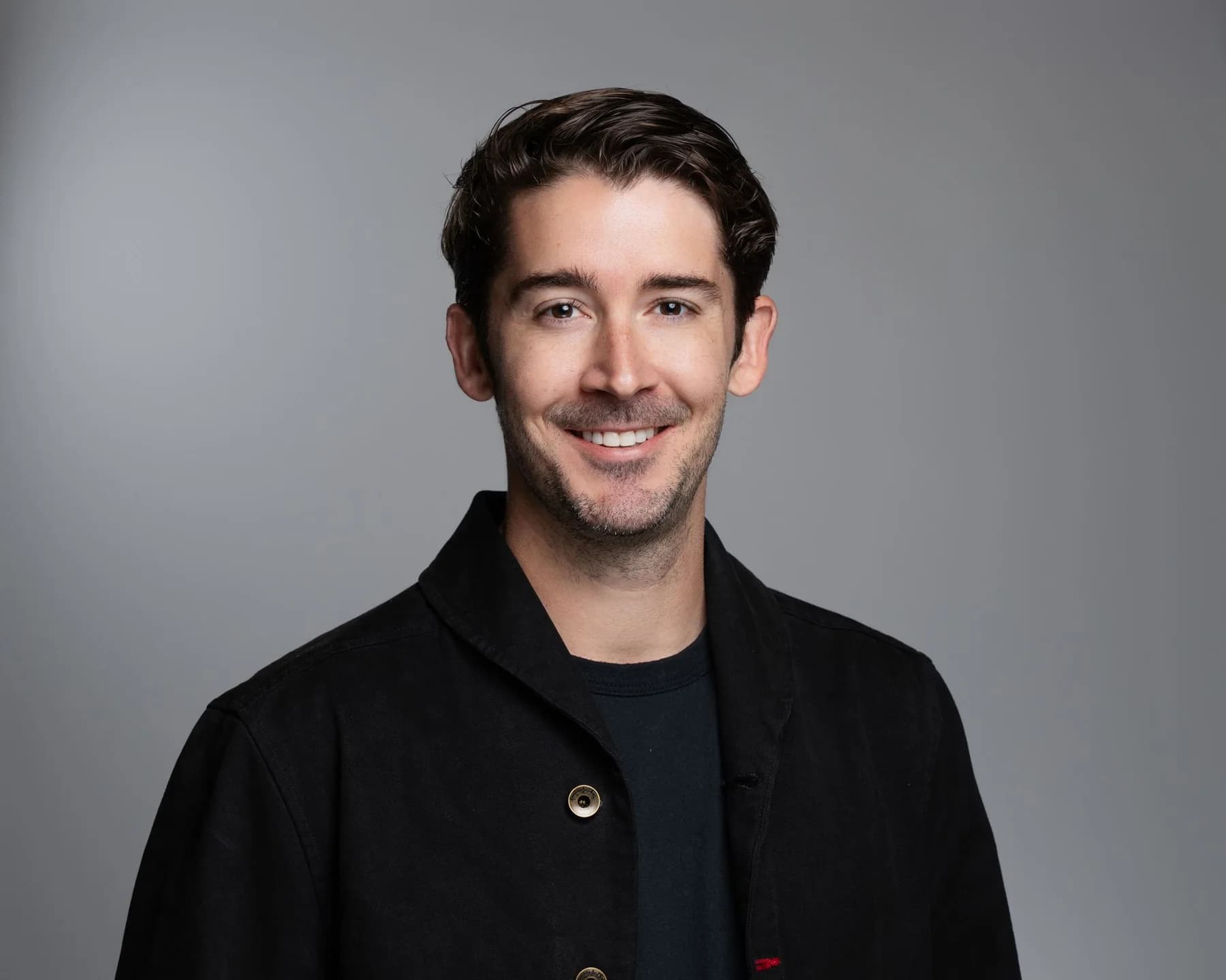 Male team member in a black shirt against a gray studio backdrop