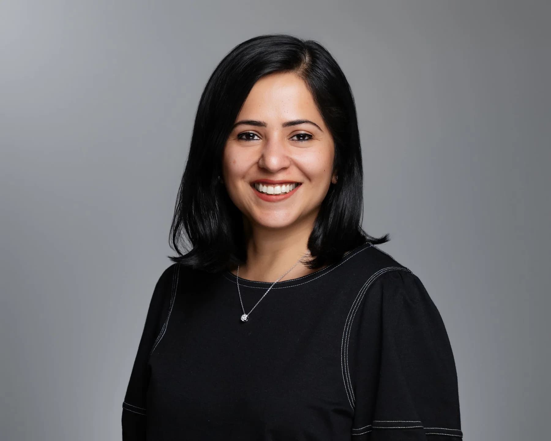 Smiling female team member in a black top against a gray studio backdrop