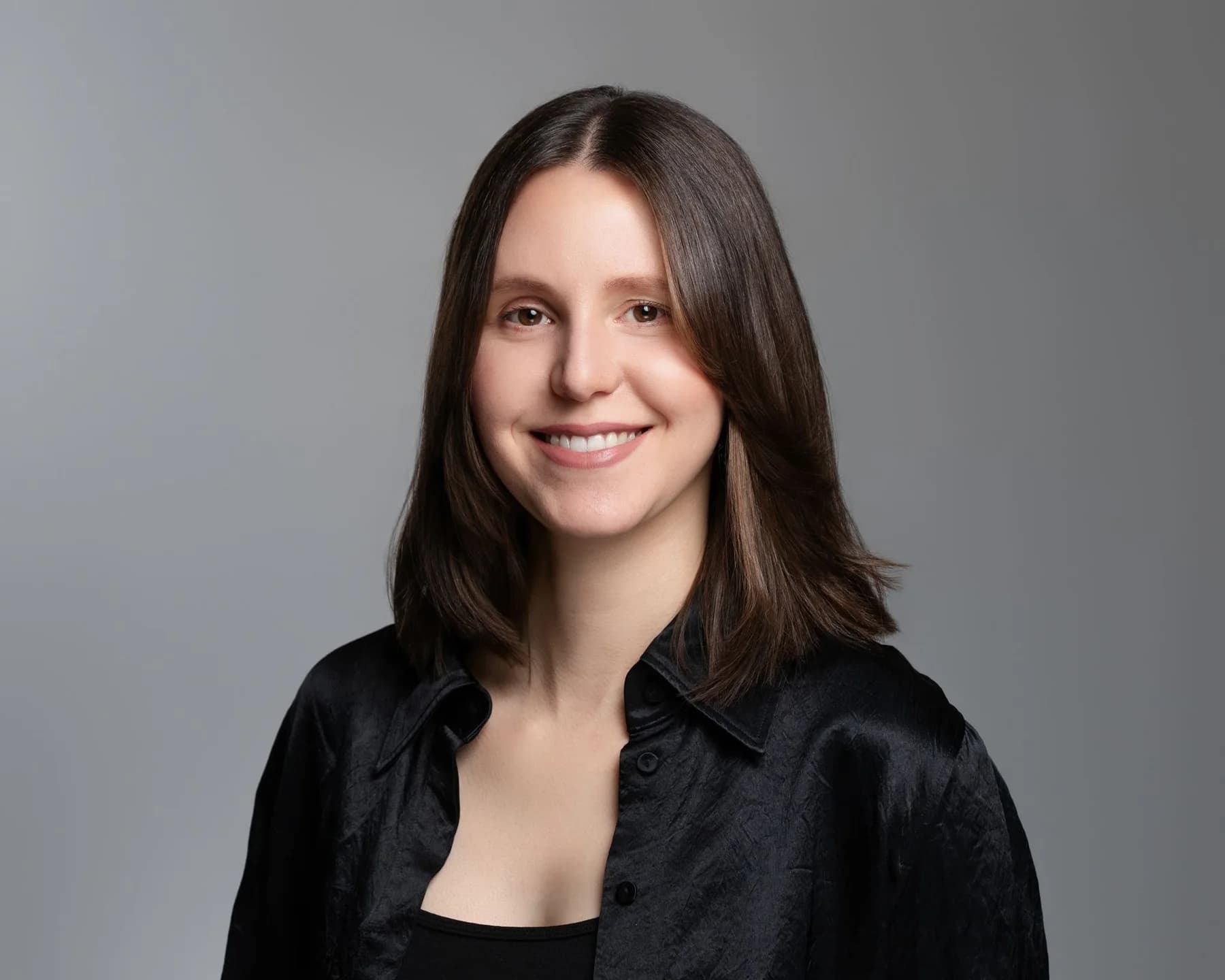 Female team member with shoulder-length brown hair against a gray studio backdrop