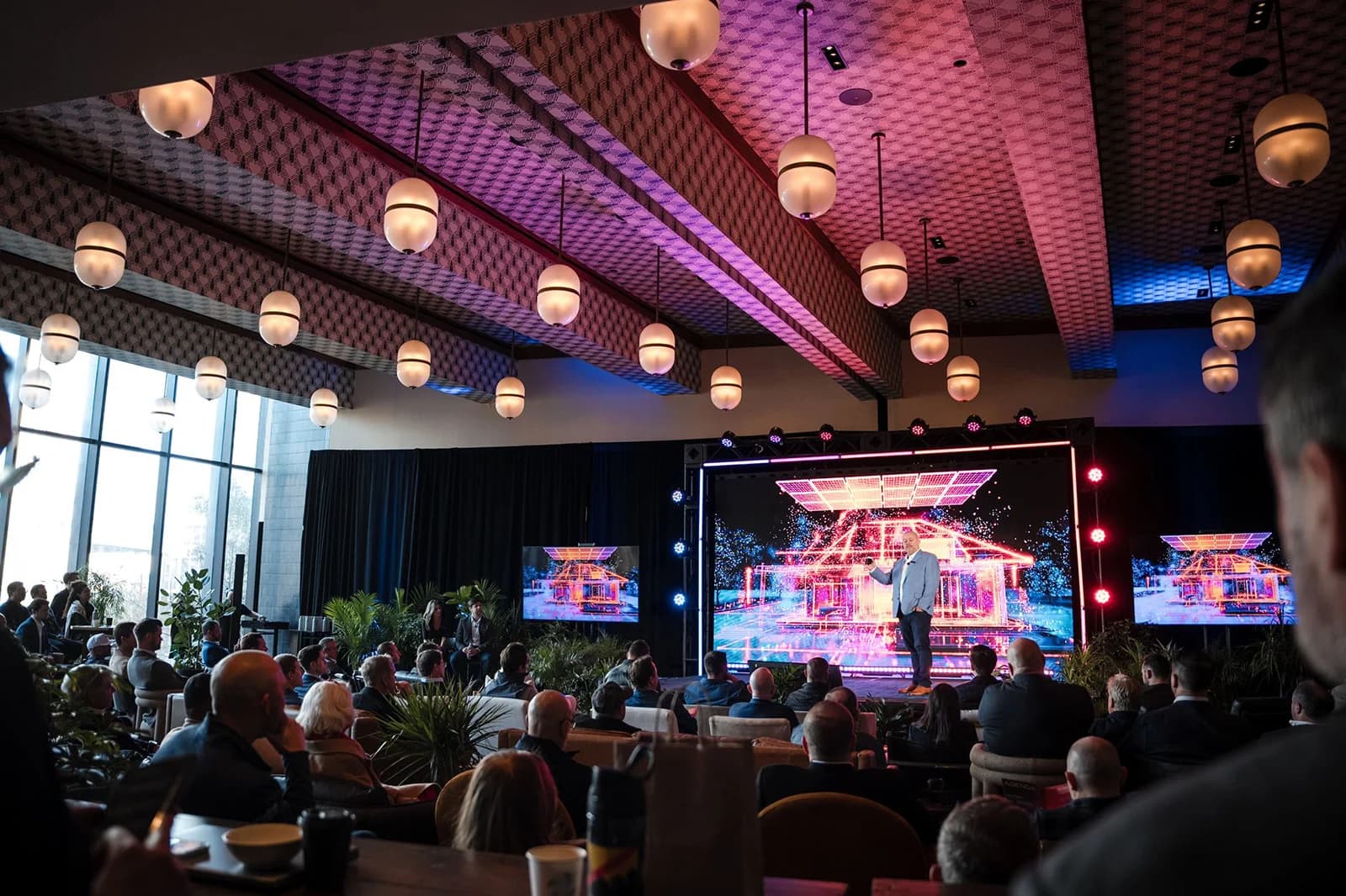 Conference audience facing a brightly lit stage beneath rows of hanging lanterns
