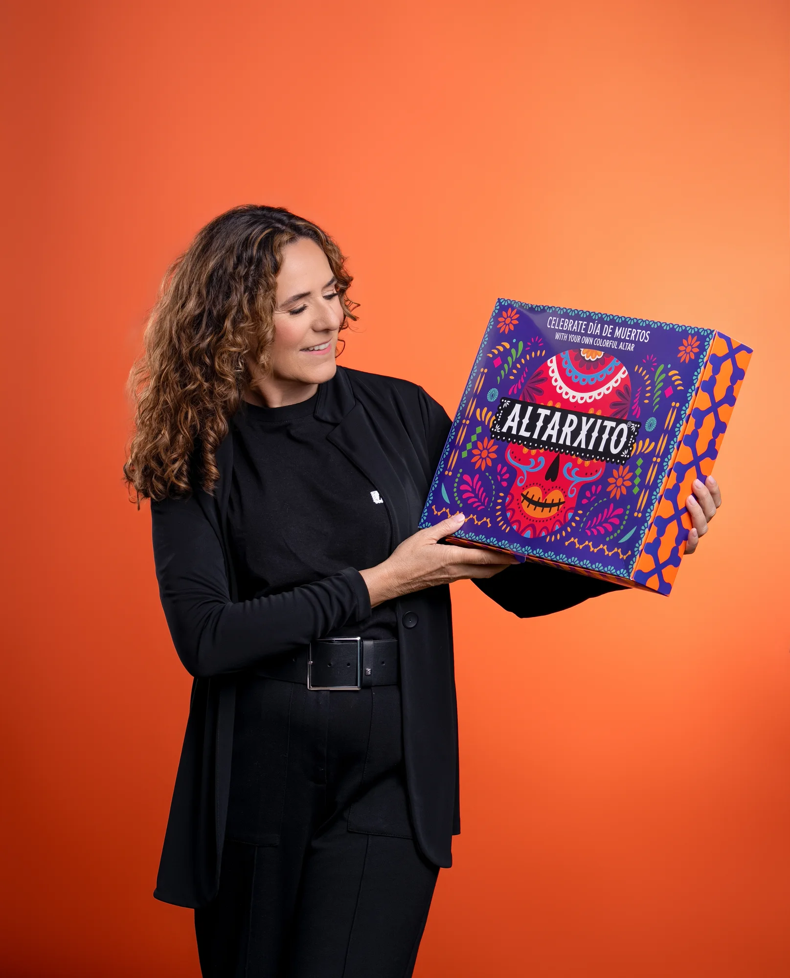 Woman holding a purple Altarxito product box against an orange studio backdrop